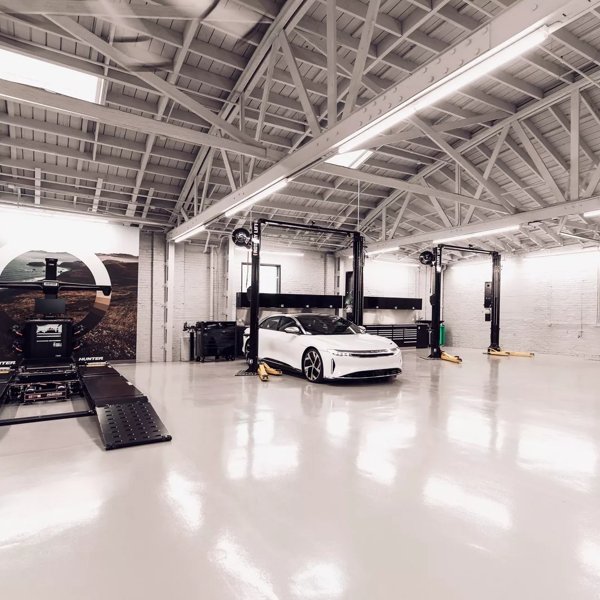 A Stellar White Metallic Lucid Air is parked inside of a Lucid service center. The floor is clean and shiny, reflecting the lights above.